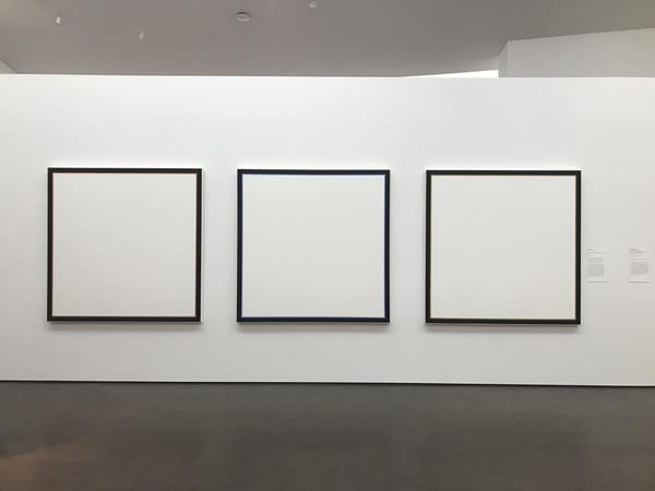 A white gallery wall with three pictures, each square, each totally white with black frames.