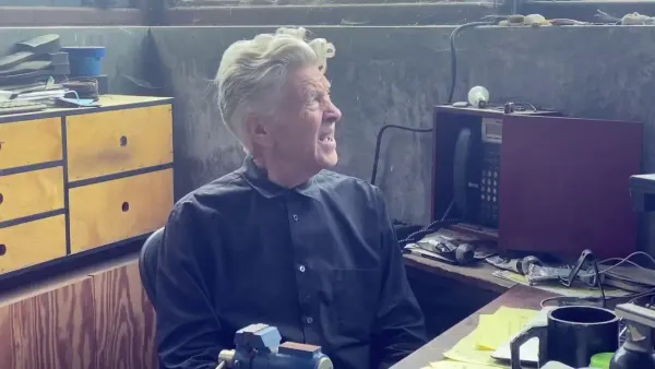 David Lynch sitting at a desk, looking out the window with a confused or concerned look on his face.